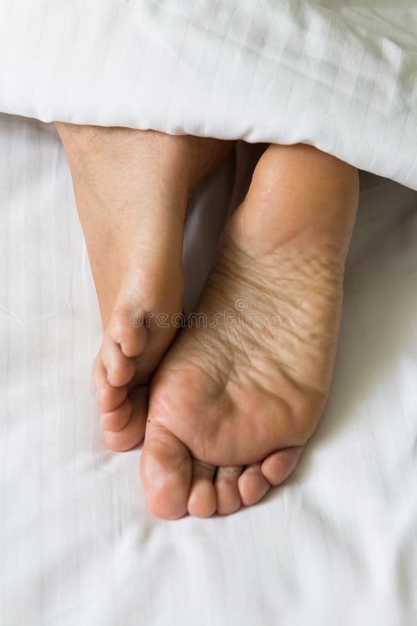 Feet of human legs protrude from under the blanket. stock photo Feet of human legs protrude from under the blanket. stock photo