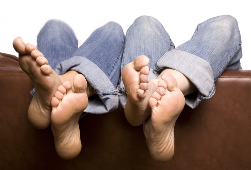 Two pairs of feet with ankles crossed and hanging over the back of the couch relaxing with their jeans rolled up. Two pairs of feet with ankles crossed and hanging over the back of the couch relaxing with their jeans rolled up.