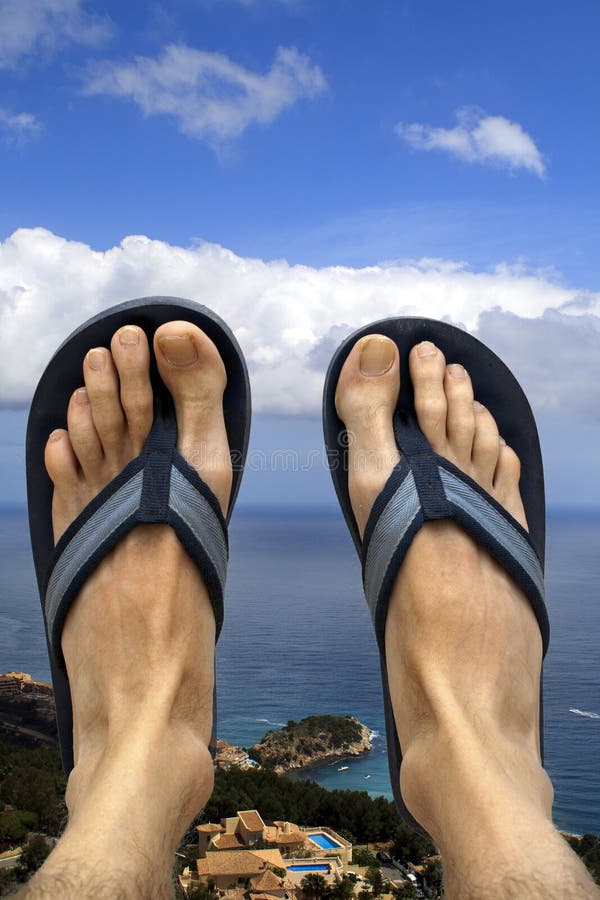 Feet wearing flip flops/ beach sandals relaxing overlooking the coastine and ocean. Feet wearing flip flops/ beach sandals relaxing overlooking the coastine and ocean