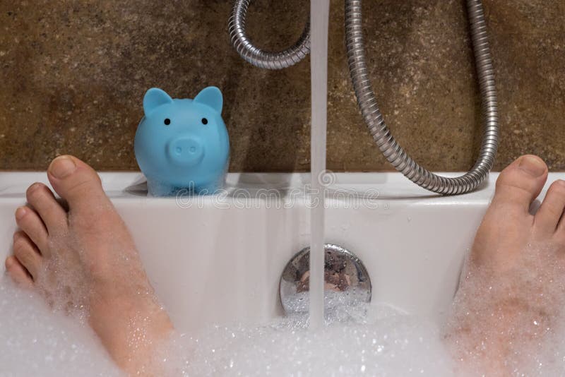 Feet sticking out of the bathtub full of water and a piggy bank. concept of cost of consumption and water waste