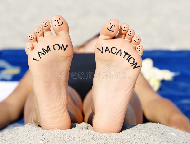 Woman showing bare feet on beach blanket with smiley faces on toes and text I am on vacation in sunshine. Woman showing bare feet on beach blanket with smiley faces on toes and text I am on vacation in sunshine.