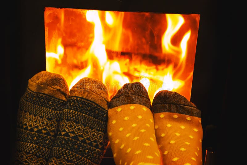 Feet in wool socks of couple lovers warming by cozy fire. stock images