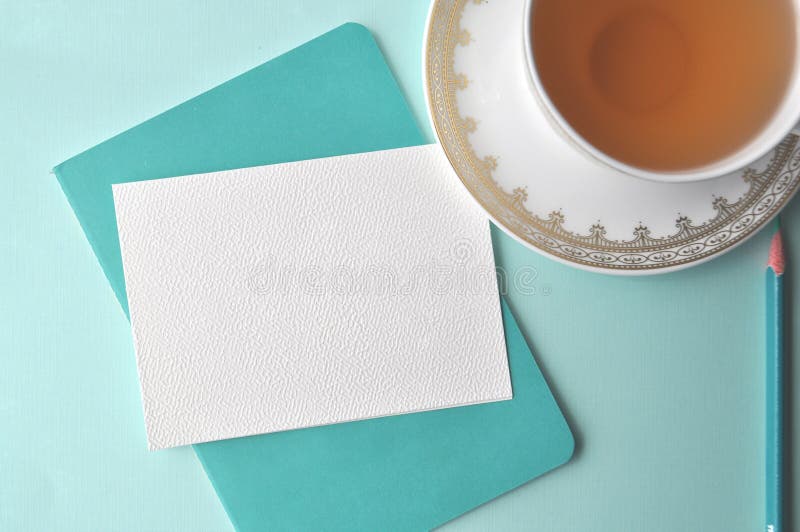 Fine white porcelain china cup with tea, teal pencil, white note card and aqua mint pale blue background with copy space. Fine white porcelain china cup with tea, teal pencil, white note card and aqua mint pale blue background with copy space