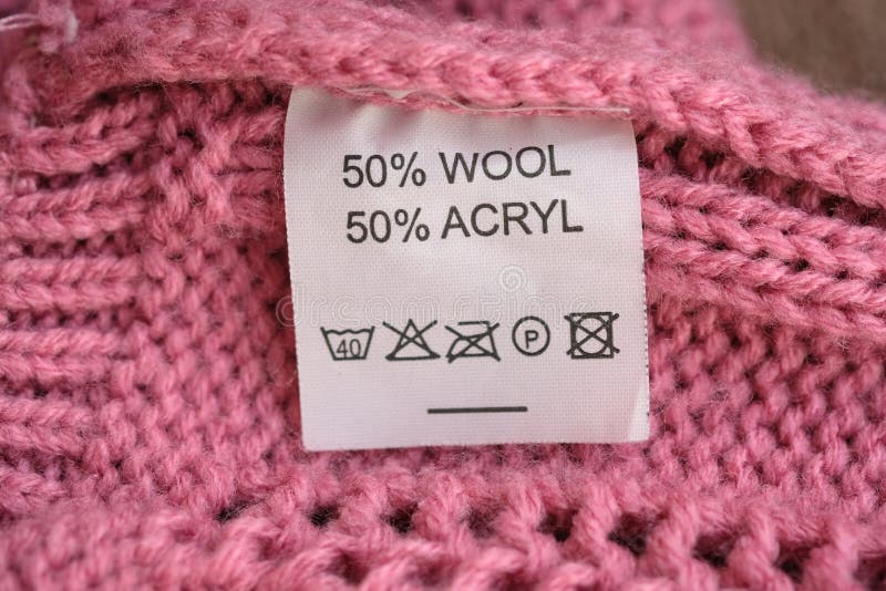 Wrong side of a pink knitted sweater made of wool, the composition is specified: 50% wool and 50% acryl. Fabric composition white clothes label on pink texture background. Wrong side of a pink knitted sweater made of wool, the composition is specified: 50% wool and 50% acryl. Fabric composition white clothes label on pink texture background