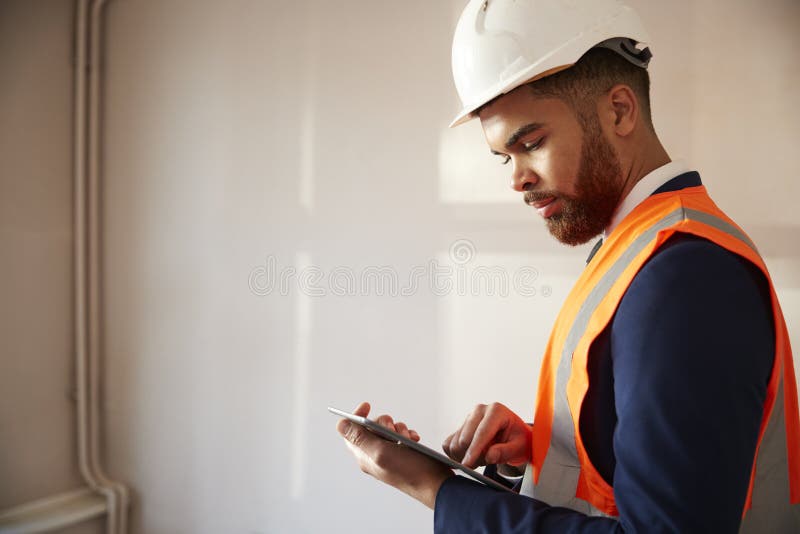 Surveyor In Hard Hat And High Visibility Jacket With Digital Tablet Carrying Out House Inspection. Surveyor In Hard Hat And High Visibility Jacket With Digital Tablet Carrying Out House Inspection