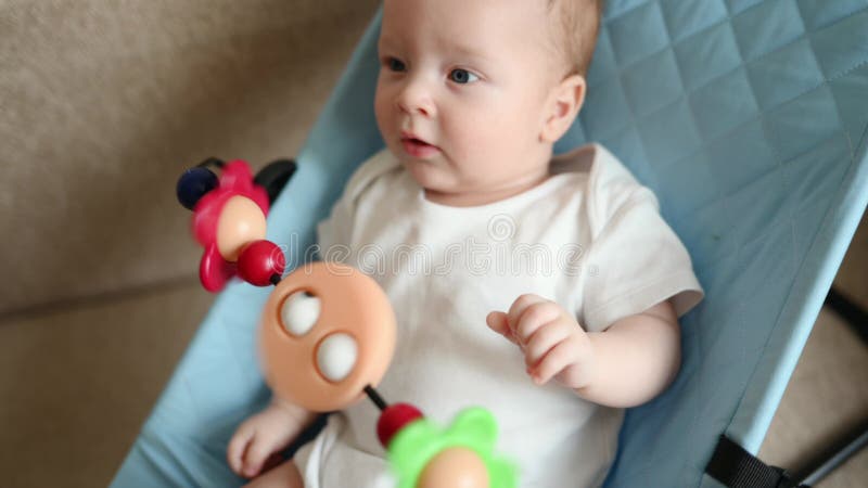 Felice bambino è sdraiato su una sega per bambini chaise lounge mentre filtra giocattoli su un bambino che sorride e video d archivio