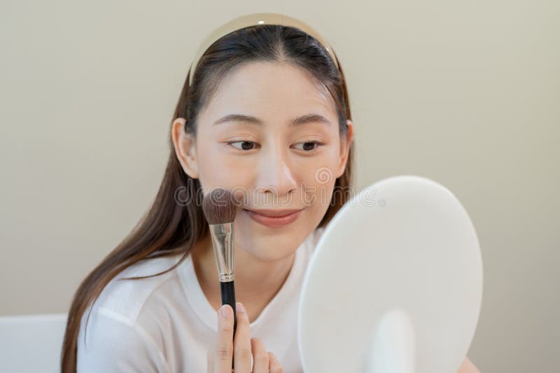 Felice concetto di bellezza di routine, una giovane ragazza carina e asiatica si trucca in faccia applicando una fondazione in pol