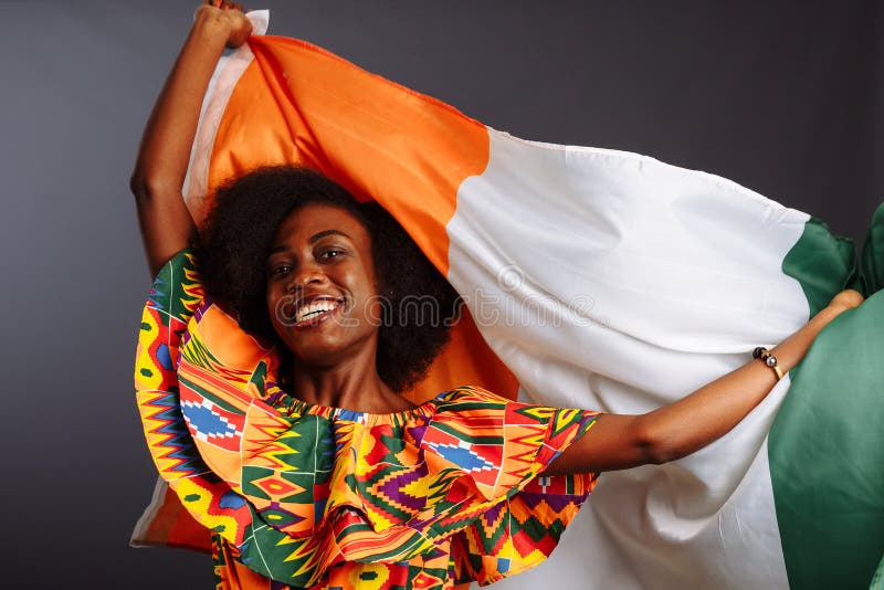 Felice donna africana in abiti nazionali, sorridente e in posa con una bandiera Costa d'Avorio, Costa d'Avorio isolata per un gri