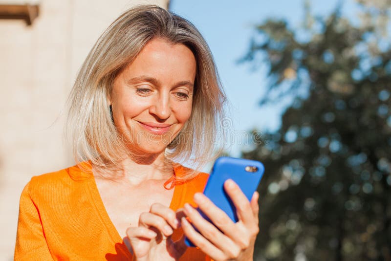 Felice donna di mezza età fuori città col cellulare immagine stock libera da diritti