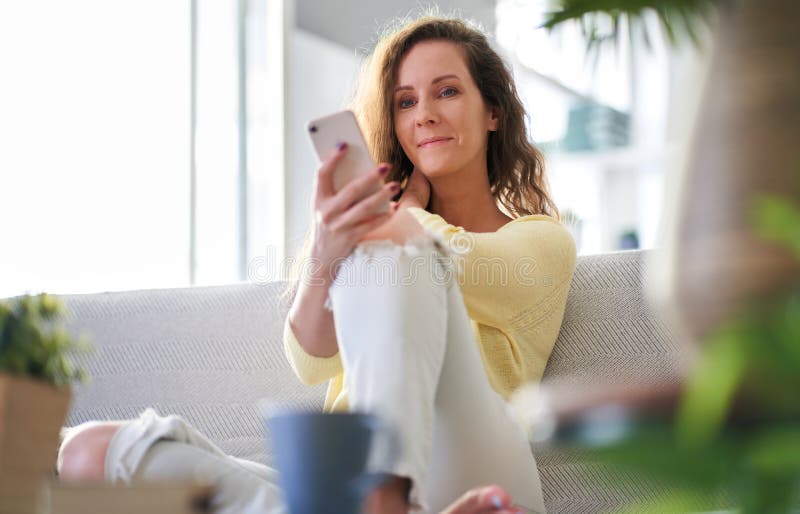 Happy smiling woman using phone sitting on sofa at home in the living room. Happy smiling woman using phone sitting on sofa at home in the living room.