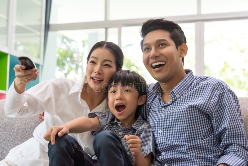 Felice famiglia asiatica che guarda la televisione insieme sul divano in salotto concetto familiare e familiare fotografie stock Felice famiglia asiatica che guarda la televisione insieme sul divano in salotto concetto familiare e familiare fotografie stock