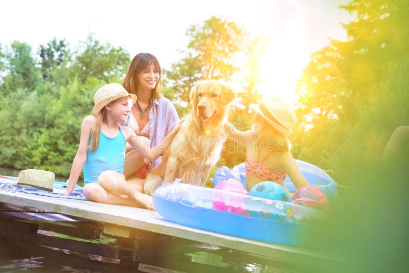Felice famiglia seduta al molo a lakeshore con il loro cane fotografia stock libera da diritti Felice famiglia seduta al molo a lakeshore con il loro cane fotografia stock libera da diritti