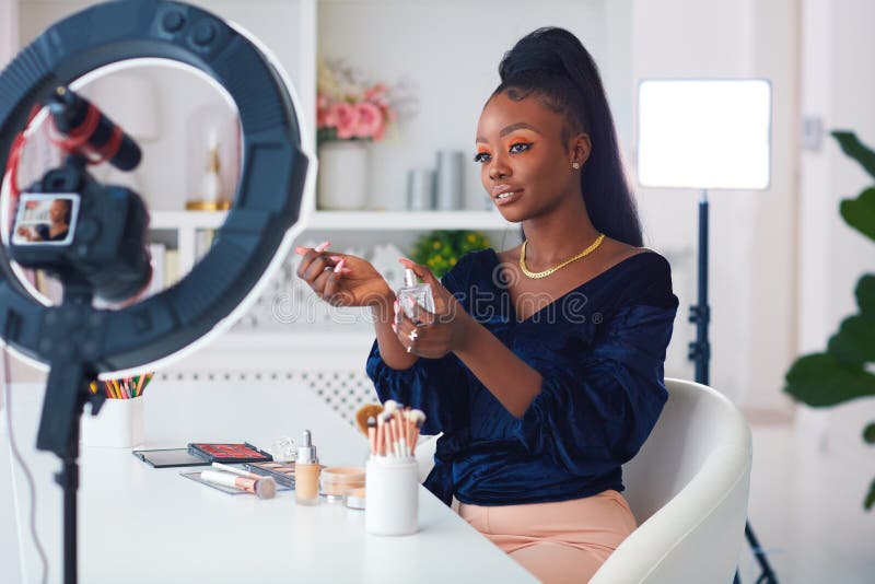 Felice giovane afro-americana donna che trascina un blog di bellezza dal creatore di contenuti online a casa, applicando un profum