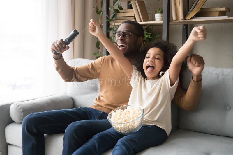 Felice papà nero e figlia che applaudono mentre guardano il calcio in TV