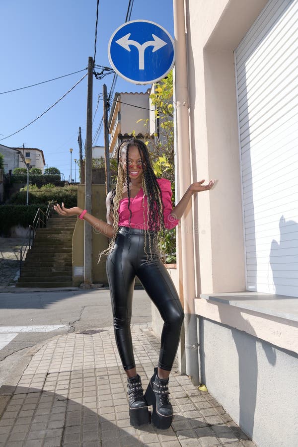 Felice ragazza nera in stile afro con lunghe trecce nere e bionde e occhiali da sole sorride mentre guarda la telecamera accanto fotografia stock libera da diritti Felice ragazza nera in stile afro con lunghe trecce nere e bionde e occhiali da sole sorride mentre guarda la telecamera accanto fotografia stock libera da diritti