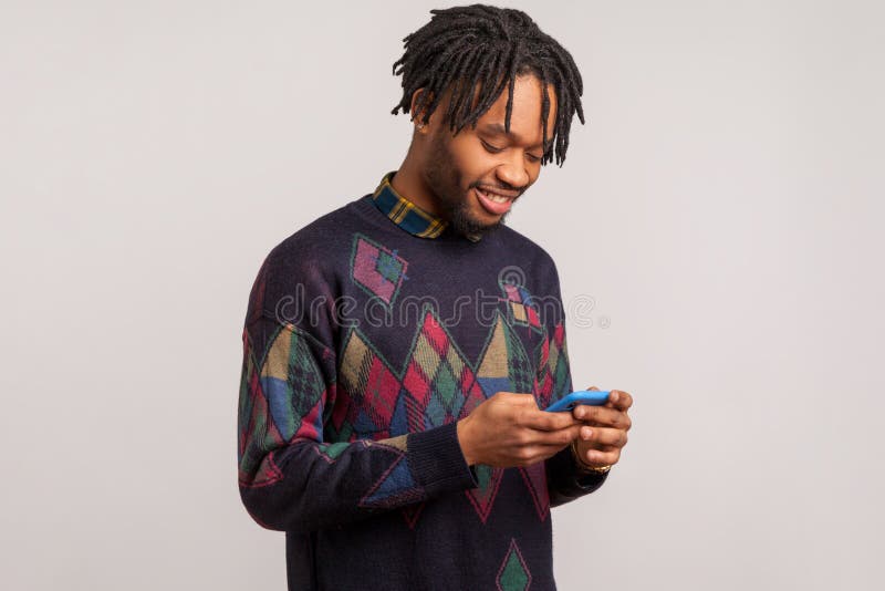 Felice uomo africano soddisfatto, con le lancette in stile casual che chiacchiera smartphone con un sorriso di puzza in faccia, f fotografie stock