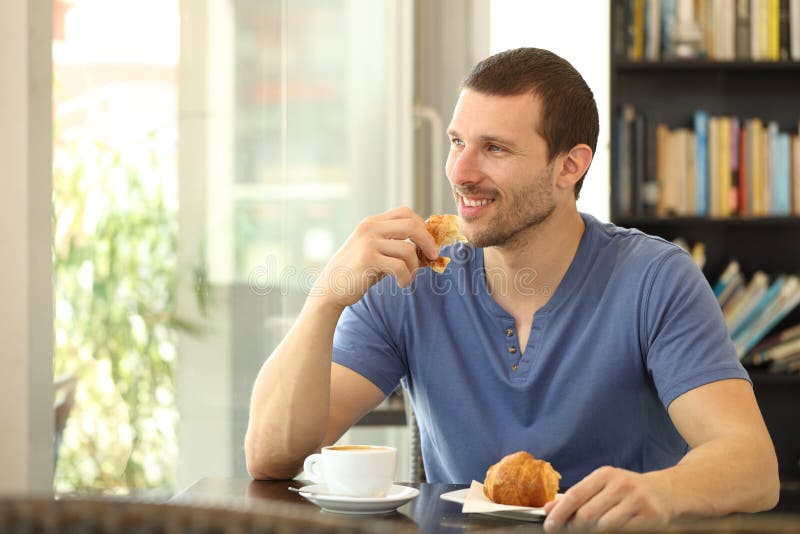 Felice uomo che mangia un cornetto per colazione in una caffetteria
