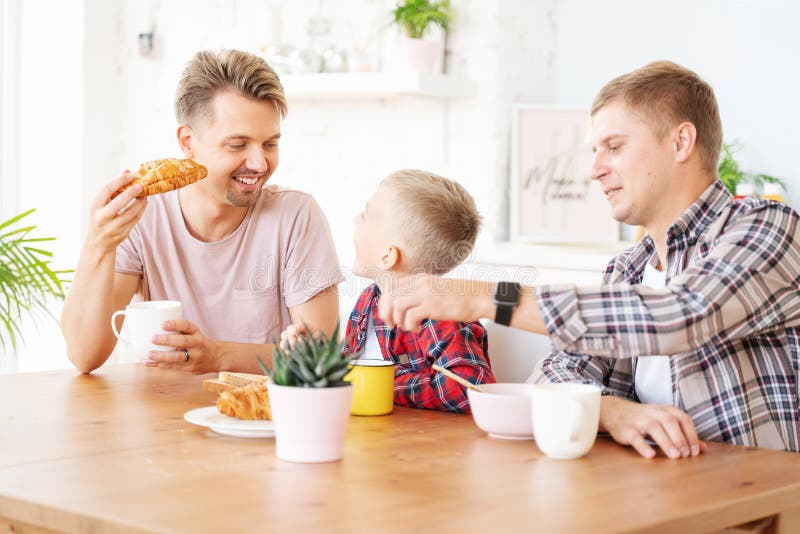 Happy young fathers and son have breakfast in the kitchen, gay family with a child, time together, parenting in homosexual families concept. Happy young fathers and son have breakfast in the kitchen, gay family with a child, time together, parenting in homosexual families concept.