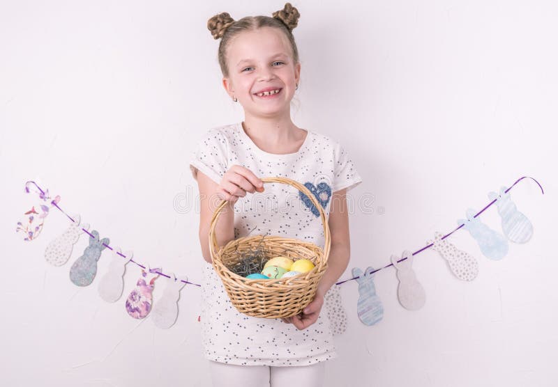 Felicitações na Páscoa feliz: a menina está guardando uma cesta com os ovos pintados pela parede branca fotografia de stock Felicitações na Páscoa feliz: a menina está guardando uma cesta com os ovos pintados pela parede branca fotografia de stock
