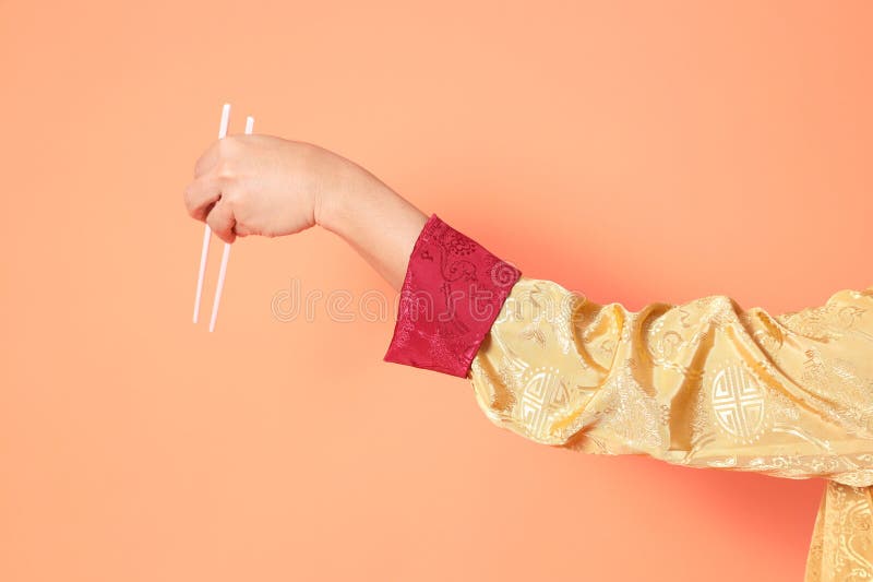 Happy Chinese new year. asian chinese senior man wearing golden traditional cheongsam qipao or changshan dress with gesture of hand holding white chopsticks isolated on orange background. Happy Chinese new year. asian chinese senior man wearing golden traditional cheongsam qipao or changshan dress with gesture of hand holding white chopsticks isolated on orange background