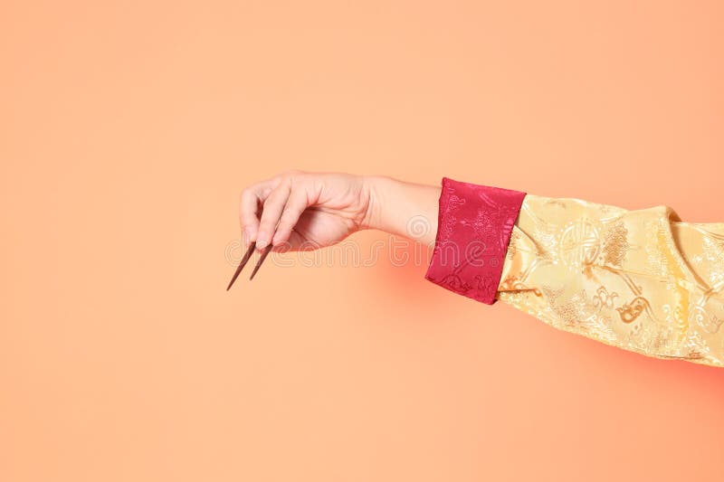 Happy Chinese new year. asian chinese senior man wearing golden traditional cheongsam qipao or changshan dress with gesture of hand holding brown chopsticks isolated on orange background. Happy Chinese new year. asian chinese senior man wearing golden traditional cheongsam qipao or changshan dress with gesture of hand holding brown chopsticks isolated on orange background