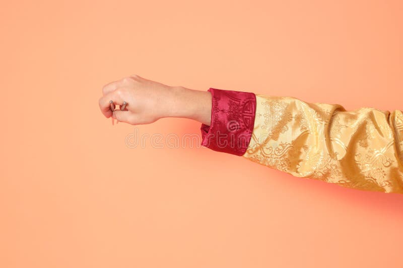 Happy Chinese new year. asian chinese senior man wearing golden traditional cheongsam qipao or changshan dress with gesture of hand holding silver chopsticks isolated on orange background. Happy Chinese new year. asian chinese senior man wearing golden traditional cheongsam qipao or changshan dress with gesture of hand holding silver chopsticks isolated on orange background