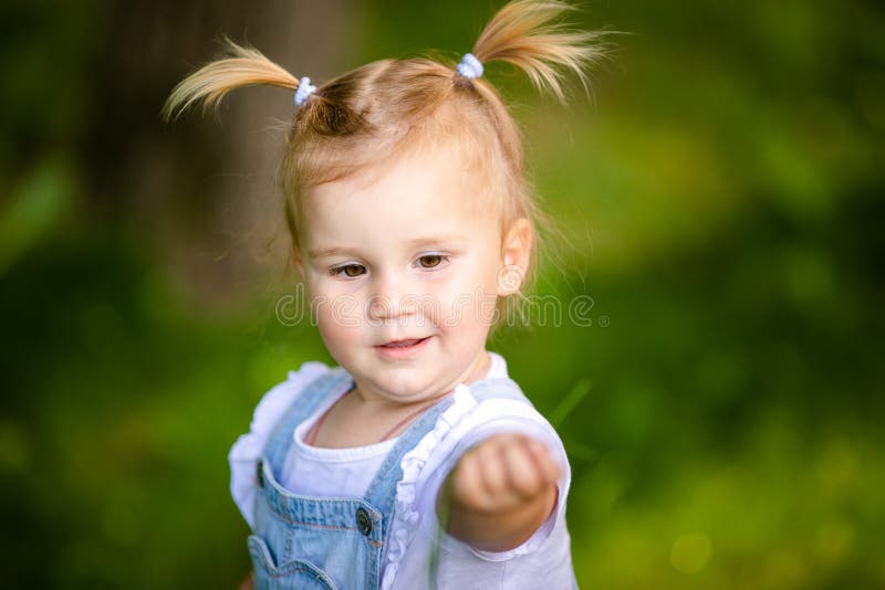 Feliz Bebê Loira Com Duas Pequenas Tranças Em Camiseta Branca E Um Kit De  Calças Jeans Sentado Sobre O Fundo Da Grama Verde Foto de Stock - Imagem de  pouco, inocência: 143643548