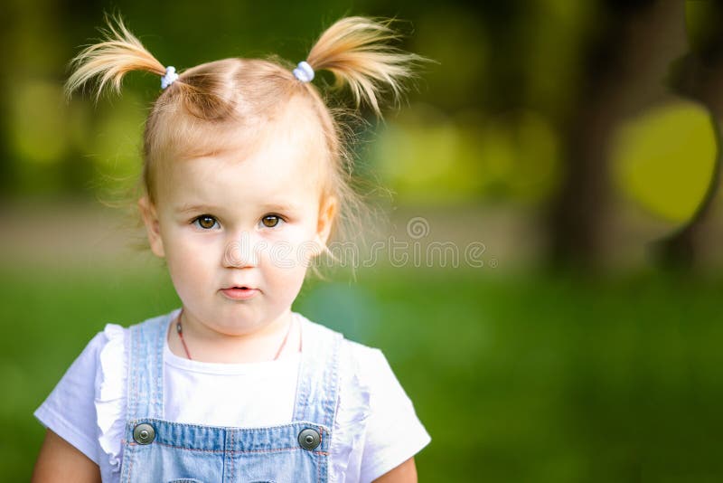 Feliz Bebê Loira Com Duas Pequenas Tranças Em Camiseta Branca E Um Kit De  Calças Jeans Sentado Sobre O Fundo Da Grama Verde Foto de Stock - Imagem de  pouco, inocência: 143643548