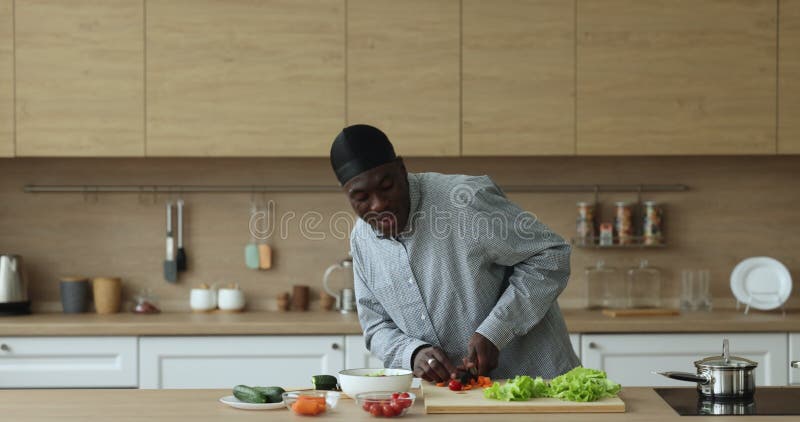 Feliz cocinero africano hombre en sombrero para cortar verduras