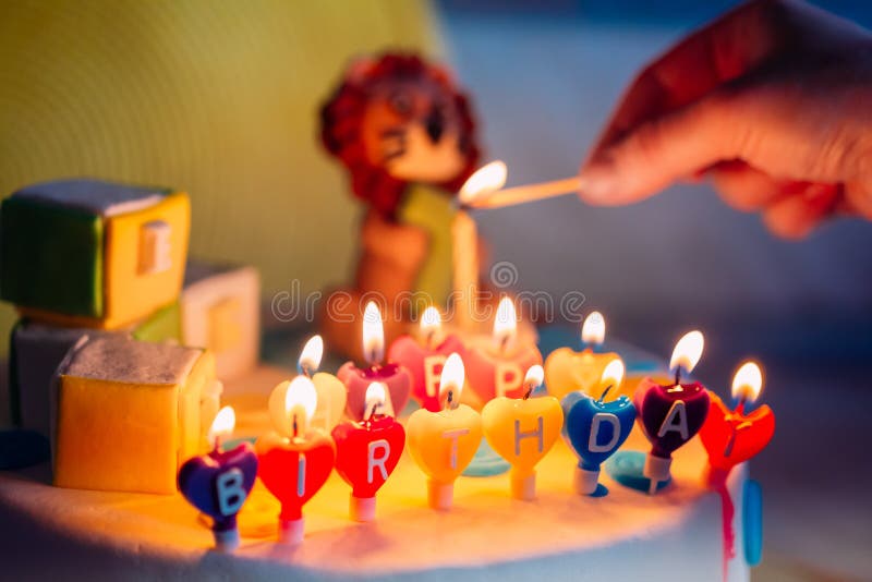 Feliz cumpleaños escrito en velas del Lit en la torta colorida Mano que lleva a cabo un partido de madera que iluminación imagenes de archivo Feliz cumpleaños escrito en velas del Lit en la torta colorida Mano que lleva a cabo un partido de madera que iluminación imagenes de archivo