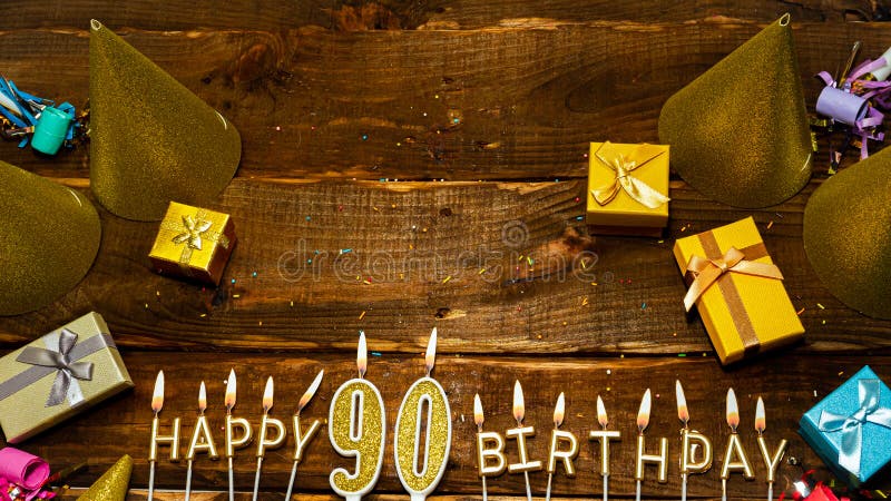 Top view of the golden letters of the candle with the number happy birthday, the background of the gift boxes with candles happy birthday on the background of brown boards. Copy space Postcard Happy birthday 90. Top view of the golden letters of the candle with the number happy birthday, the background of the gift boxes with candles happy birthday on the background of brown boards. Copy space Postcard Happy birthday 90