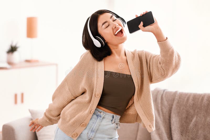 Feliz dama asiática cantando usando el smartphone como micrófono fotos de archivo libres de regalías