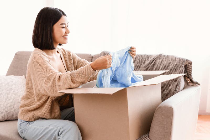 Feliz dama asiática desempacando ropa luego de comprar en línea fotos de archivo