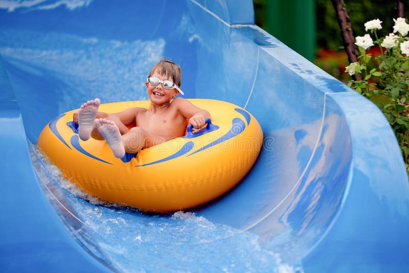Feliz de que un niño de 8 años esté en el parque acuático en círculos inflables sobre toboganes de agua con salpicaduras fotos de archivo