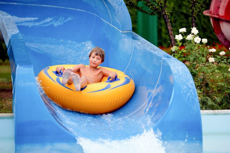 Feliz de que un niño de 8 años esté en el parque acuático en círculos inflables sobre toboganes de agua con salpicaduras fotos de archivo libres de regalías