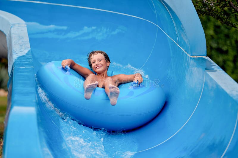 Feliz de que un niño de 8 años esté en el parque acuático en círculos inflables sobre toboganes de agua con salpicaduras fotos de archivo