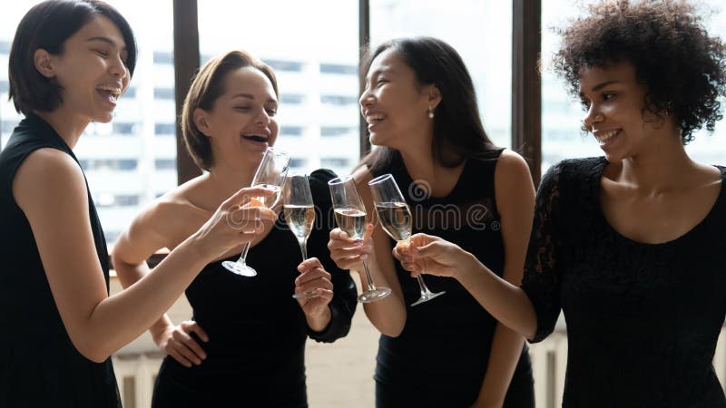 Feliz diversa mujeres que llevan vestidos negros elegantes que clinking copas de champán