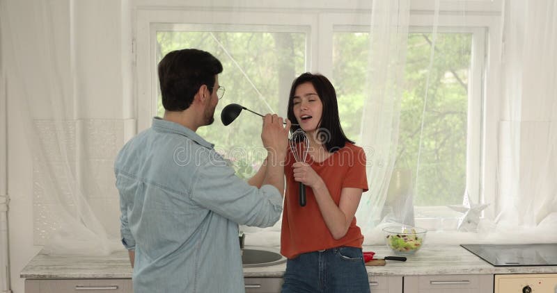 Feliz e positivo casal de famílias milenares cantando canções na cozinha.