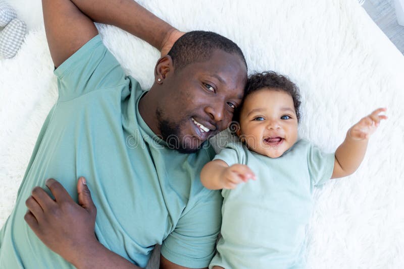 Feliz e sorridente pai africano com filho bebê na cama em casa, abraço, feliz dia dos pais da família