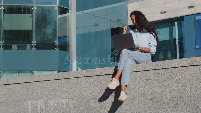 Feliz empresária freelancer estudante sentada na cidade com laptop lê boas notícias ganhando