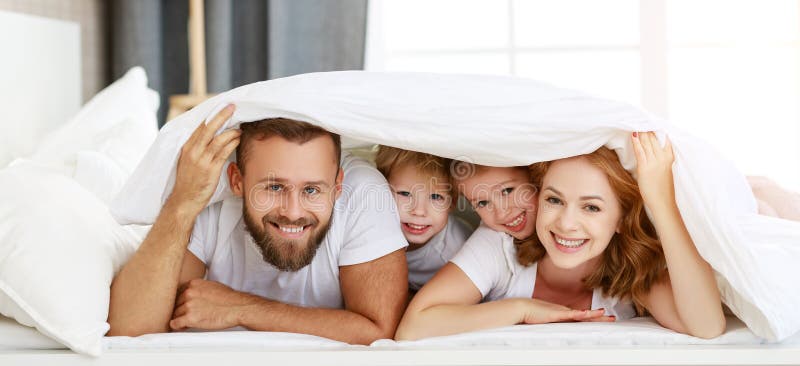 Happy family mother, father and children laughing, playing and smiling in bed in bedroom at home. Happy family mother, father and children laughing, playing and smiling in bed in bedroom at home