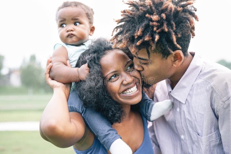 Feliz familia negra divirtiéndose en un parque al aire libre - Madre y padre con su hija disfrutando del tiempo juntos en un día foto de archivo