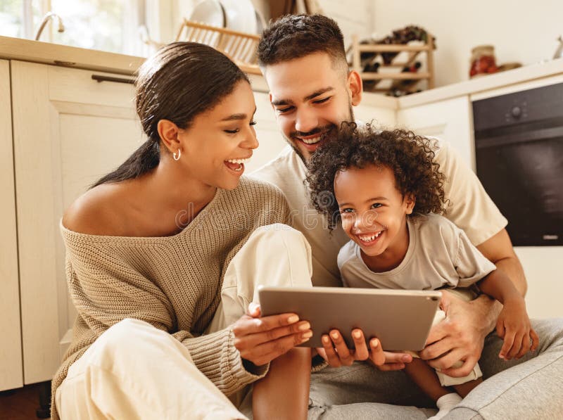 Feliz família multiétnica: pais e filho riram e assistem a um vídeo engraçado em um tablet em casa