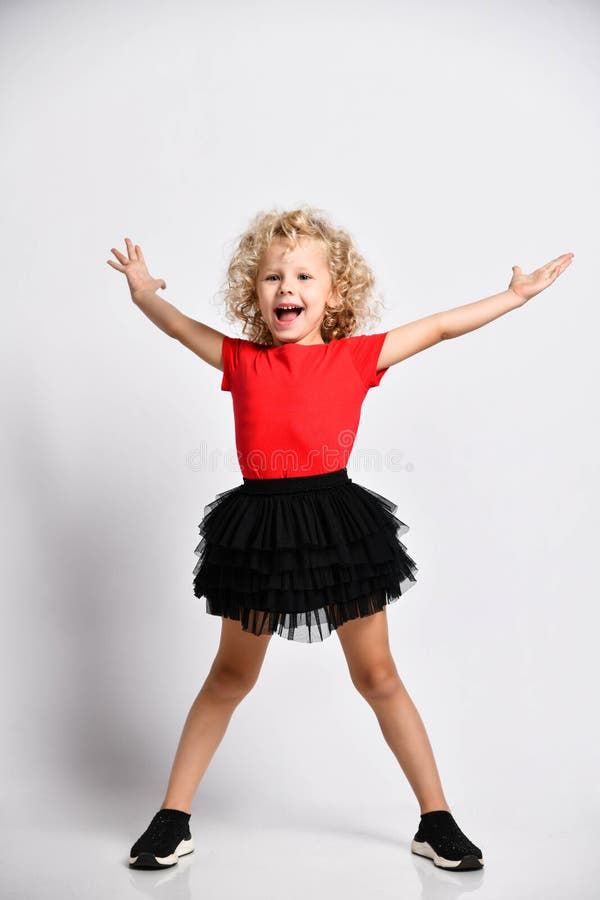 Linda Niña Pequeña Con Falda Negra Y Camiseta Roja Se Pone De Pie Con Las  Piernas Muy Separadas Y Sosteniendo La Cabeza Foto de archivo - Imagen de  ejercicios, estallido: 178857478