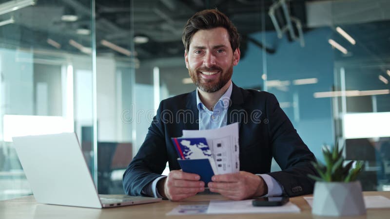 Feliz hombre de negocios sentado en el escritorio y con pasaporte con tour reservado