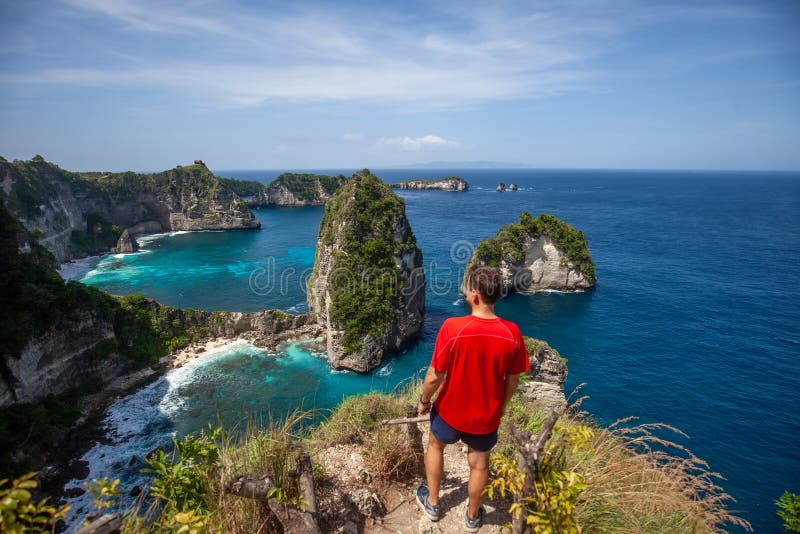 Feliz homem de pé e olhando para a rocha Mil Ilha Viewpoint Nusa Penida imagem de stock royalty free Feliz homem de pé e olhando para a rocha Mil Ilha Viewpoint Nusa Penida imagem de stock royalty free