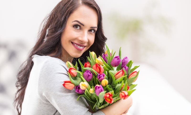 Feliz mujer de cabello oscuro sosteniendo un encantador ramo lleno de tulipanes durante el día nacional de la mujer foto de archivo libre de regalías