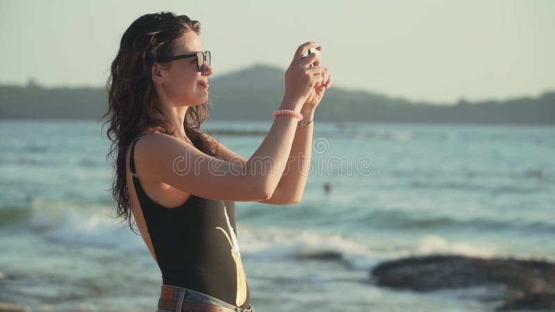 Feliz mujer toma fotos de la puesta de sol sobre el mar