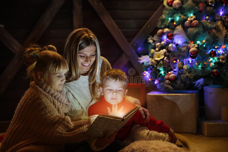 Feliz Natal e ano novo feliz Família bonita no interior do Xmas Mãe nova bonita que lê um livro a ela fotos de stock Feliz Natal e ano novo feliz Família bonita no interior do Xmas Mãe nova bonita que lê um livro a ela fotos de stock