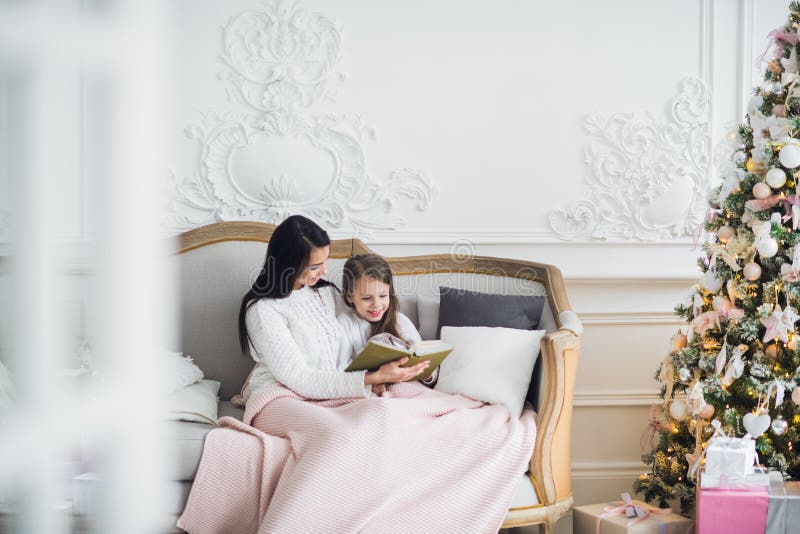 Feliz Natal e boas festas Mamã consideravelmente nova que lê um livro a sua filha bonito perto da árvore de Natal dentro imagem de stock Feliz Natal e boas festas Mamã consideravelmente nova que lê um livro a sua filha bonito perto da árvore de Natal dentro imagem de stock